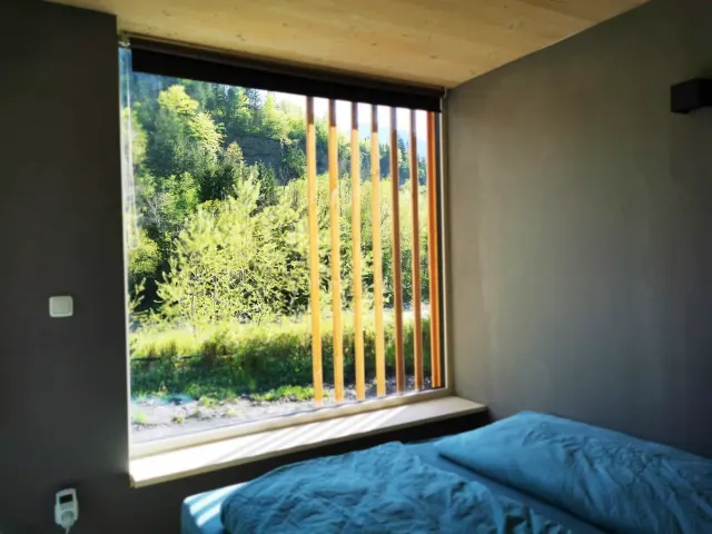 BookNoFees tatil evi: Hieflau, Styria, Avusturya – Mavi yatak takımlı ve ormana bakan ahşap panjurlu büyük pencereli yatak odası